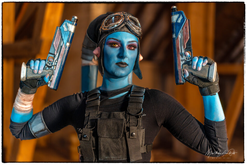 Cosplayerin im Stil von Gamora mit grüner Haut und zwei Sci-Fi-Waffen – energiegeladene Pose im Dachgeschoss.