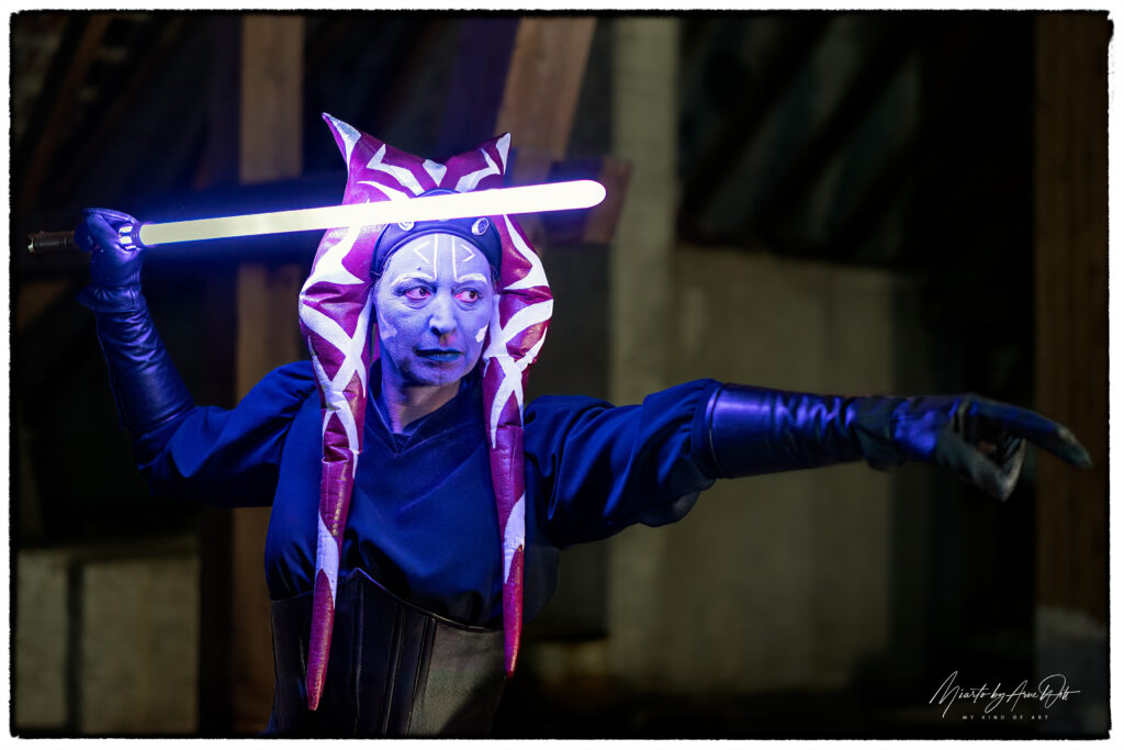 Außergewöhnliches Alien-Cosplay mit violettem Lichtschwert – leuchtende Hörner und intensiver Blick.