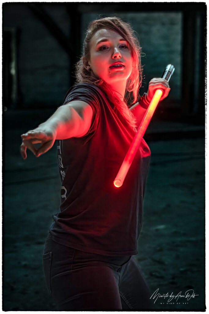 Kämpferin mit rotem Lichtschwert in Angriffsstellung – entschlossener Ausdruck im Low-Light-Setting.