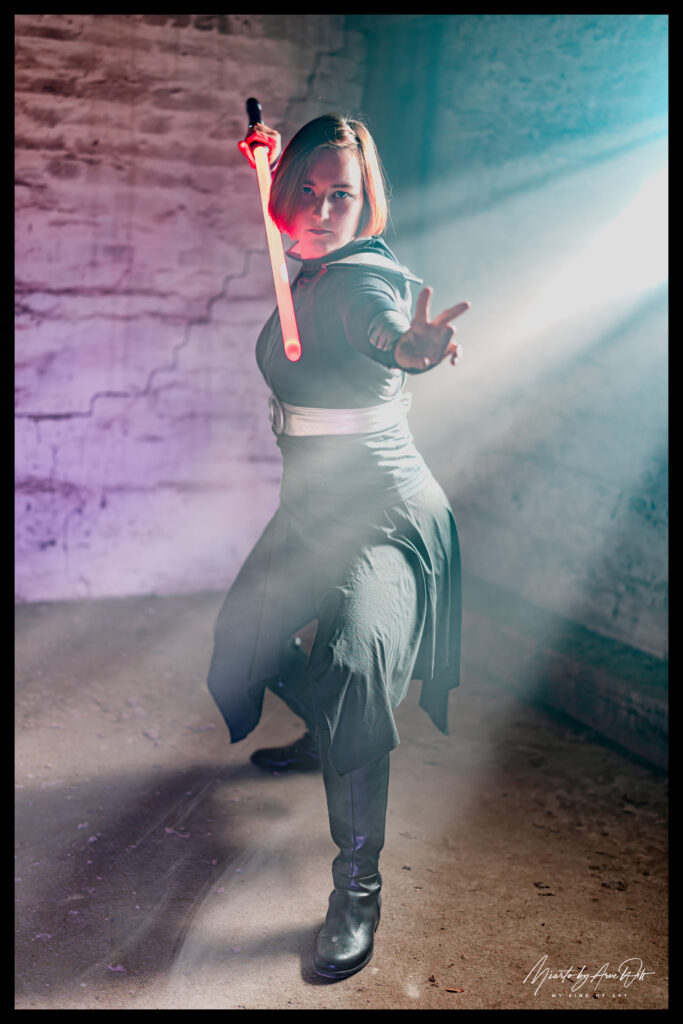 Cosplayerin in Kampfpose mit rotem Lichtschwert, farbenfroher Nebel umgibt die Szene.