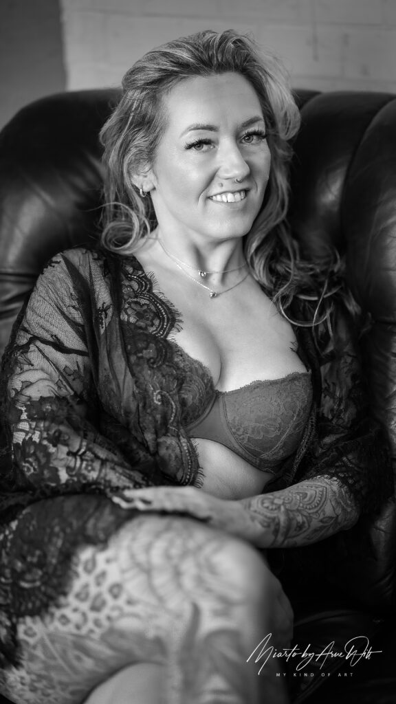 Sinnliche Boudoir-Szene: Frau in schwarzer Lingerie lächelt auf einem Sofa – natürliches Licht.