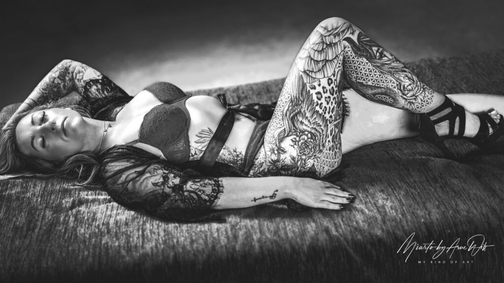 Schwarzweiß-Boudoir-Foto: Frau in Spitzenwäsche liegt entspannt auf dem Bett.