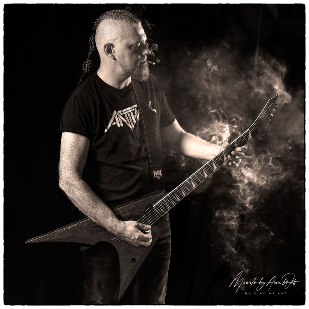 Rockmusiker mit E-Gitarre in Bühnennebel, atmosphärische Studioaufnahme